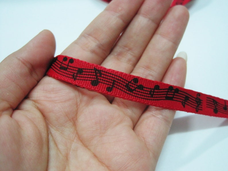 May include: Red ribbon with black musical notes printed on it. The ribbon is held in a hand.