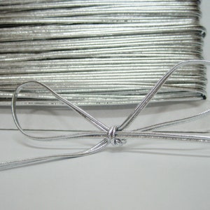 Puede incluir: Un carrete de cordón elástico plateado, con un trozo de cordón atado en forma de lazo.