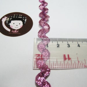 Peut inclure: Garniture m&eacute;tallique rose avec un bord ondul&eacute;, mesur&eacute;e &agrave; l'aide d'une r&egrave;gle. La garniture mesure environ 25 cm de long.