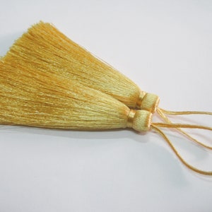 May include: Two golden yellow tassel ornaments with a loop for hanging.