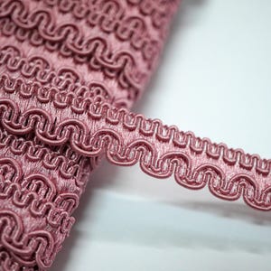 Peut inclure: Gros plan sur une garniture décorative rose avec un bord festonné. La garniture est faite d'un tissu doux et tissé et a un aspect délicat et féminin.