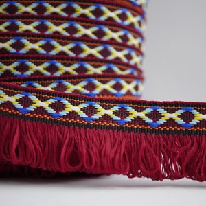 May include: Red trim with a fringe and a geometric pattern in blue, yellow, and white.