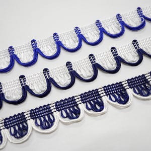 May include: Close-up of three rows of decorative trim. The trim features a white base with a scalloped edge and blue accents. The top two rows have a solid blue trim, while the bottom row has a checkered pattern.