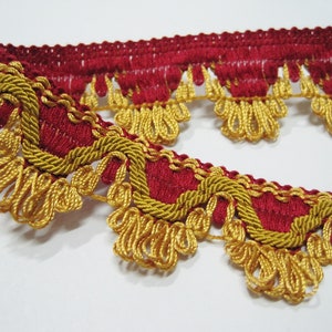 May include: Close-up of decorative trim featuring a deep red fabric base with gold-colored, looped fringe and rope-like edging. The trim is likely used for embellishing clothing, home decor, or craft projects. The design is ornate and detailed.