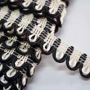 May include: Close-up of decorative trim with a scalloped edge. The trim has a woven cream base with a black border and accents. The design is intricate and detailed, suitable for craft projects.