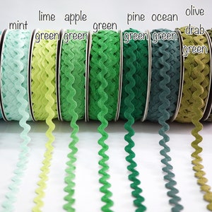 Può includere: Una collezione di rocchetti di nastro ondulato in varie tonalità di verde, dall'acqua marina al verde scuro. Ogni rocchetto è etichettato con un nome di colore, come "verde acqua", "verde menta" e "verde oliva scuro".