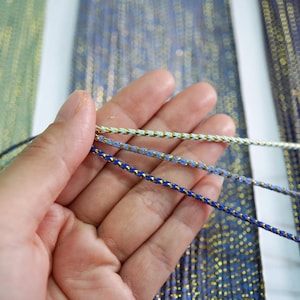 May include: Three strands of cord with a gold metallic thread running through them. The cords are light blue, medium blue, and dark blue.
