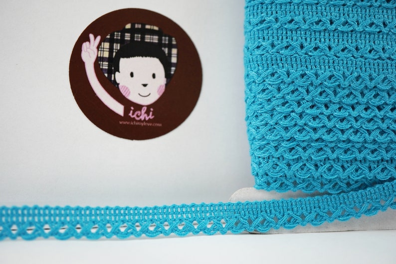 May include: Turquoise blue crochet trim with a delicate, intricate pattern. The trim is shown rolled up and laid flat.