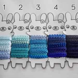 Puede incluir: Cinco carretes de encaje azul, cada uno mostrado en una tarjeta blanca en forma de conejo con un número del 1 al 5. El encaje es de varios tonos de azul, desde azul claro hasta azul oscuro.