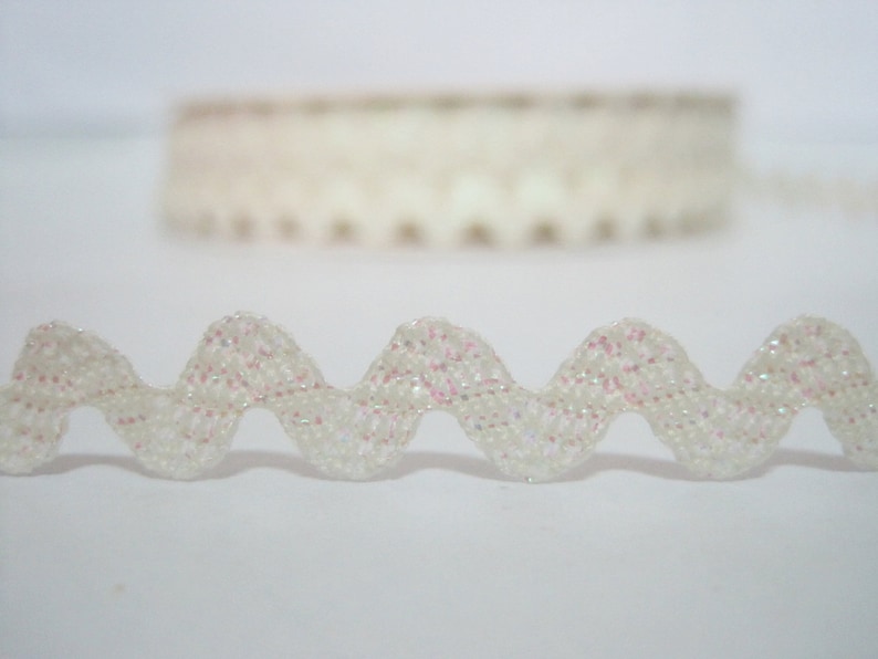 May include: White scalloped trim with iridescent glitter. The trim is wavy and has a delicate, feminine look.