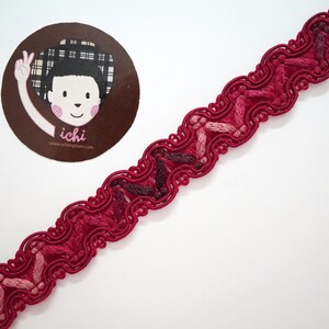 May include: Red and pink braided trim with a scalloped edge. The trim has a textured, woven look.