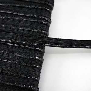 Könnte beinhalten: Schwarzes Gummiband, Nahaufnahme der flachen, gewebten Textur. Das Band ist in der Mitte gefaltet, wodurch die Breite des Bandes sichtbar wird.