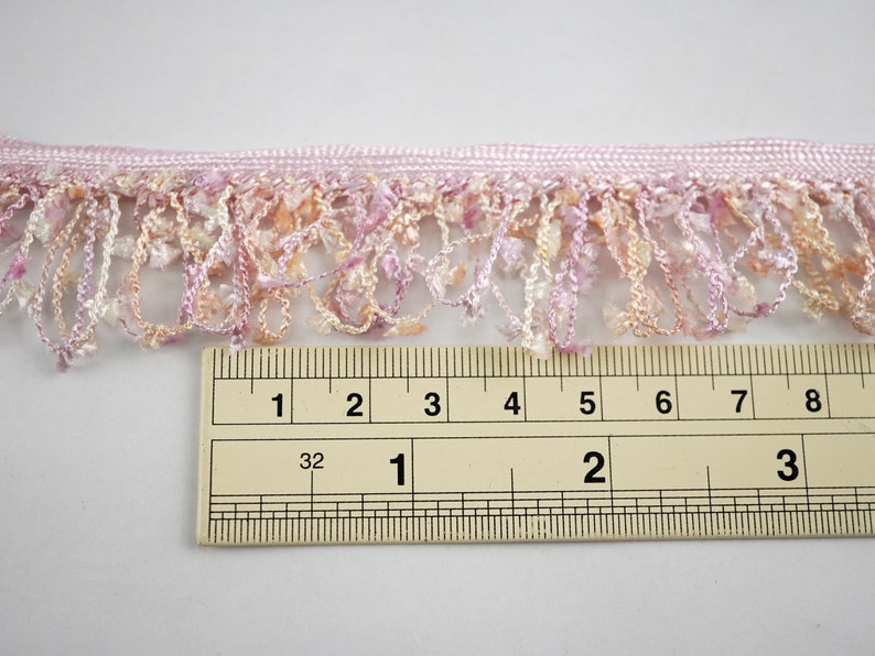 Puede incluir: Borde de flecos rosa y melocot&oacute;n con una regla que mide 5 cm de largo.