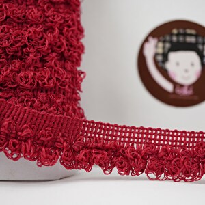May include: Red curly trim with a textured woven band. The trim is approximately 1 inch wide.