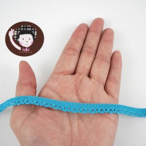 May include: A turquoise blue lace trim with a scalloped edge. The trim is about 1/2 inch wide and is shown on a hand.