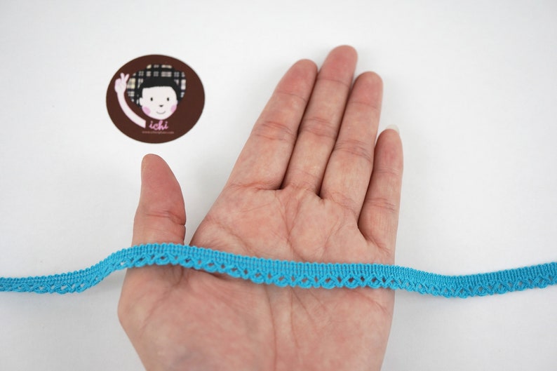 May include: A turquoise blue lace trim with a scalloped edge. The trim is about 1/2 inch wide and is shown on a hand.