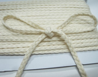 May include: A close-up of a white braided cotton cord, showing the texture and detail of the braid. The cord is tied in a bow shape.