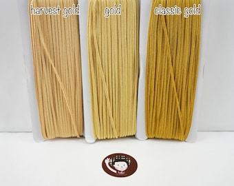 May include: Three spools of elastic cord in different shades of gold: harvest gold, gold, and classic gold.