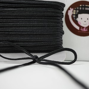May include: A spool of black elastic cord with a bow tied in the cord. The cord is wound tightly on the spool.