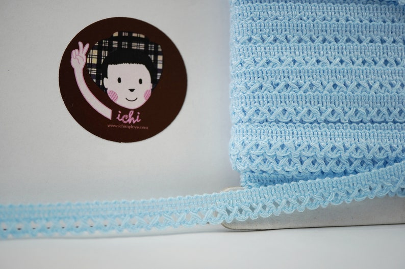 May include: Light blue crochet trim with a delicate openwork pattern. The trim is shown rolled up and laid flat. The trim is perfect for adding a touch of elegance to any project.