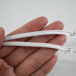 May include: Two cords of white and off-white braided cord. The cords are held in a hand, with the white cord on top and the off-white cord on the bottom. The text "white" is written next to the white cord and the text "off-white" is written next to the off-white cord.