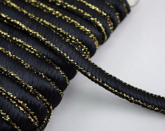 May include: Black braided trim with a gold metallic thread running through it. The trim is coiled and ready to be used for sewing or crafting projects.