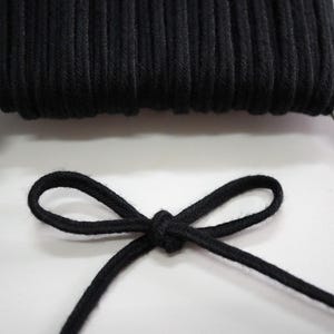 May include: Black cotton cord, wound on a spool, with a bow tied in the cord.