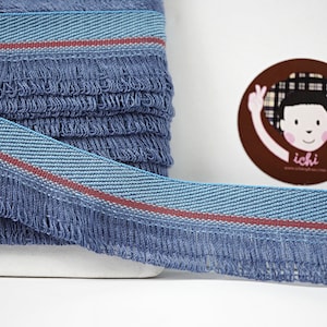 May include: Blue fringe trim with a light blue and red stripe. The trim is folded and stacked on a white surface.