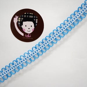 Puede incluir: Una cinta decorativa con un diseño festoneado en azul claro y blanco. La cinta está en ángulo a través del marco, con una pegatina circular con un personaje de dibujos animados en la esquina superior izquierda.