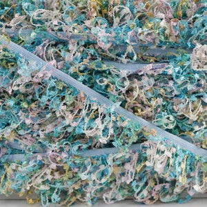 May include: A close-up of a blue, white, and green ruffled trim. The trim is made of a soft, fluffy material and has a delicate, feminine look.