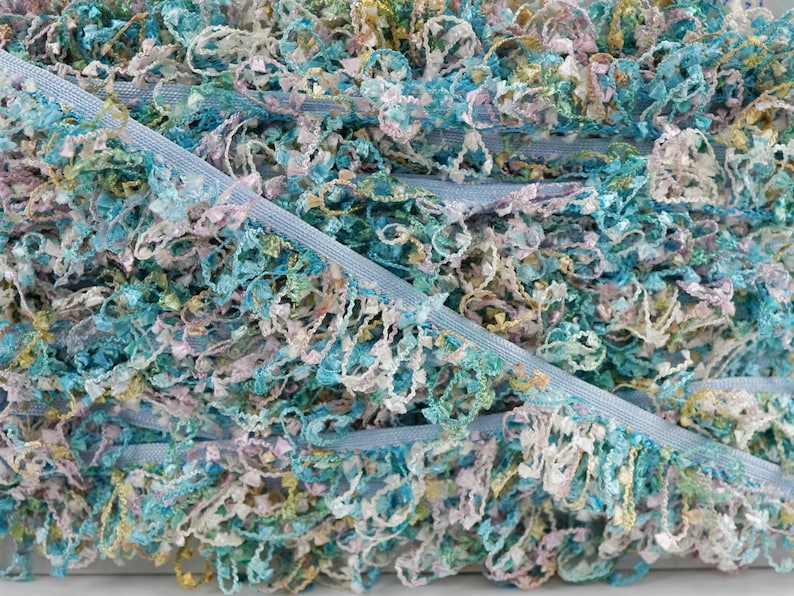 May include: A close-up of a blue, white, and green ruffled trim. The trim is made of a soft, fluffy material and has a delicate, feminine look.
