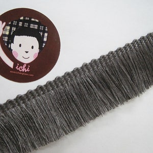 May include: Gray fringe trim with a woven texture. The fringe is about 1 inch long.