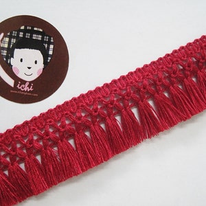 May include: Red fringe trim with a woven design. The fringe is approximately 2.5 cm long.
