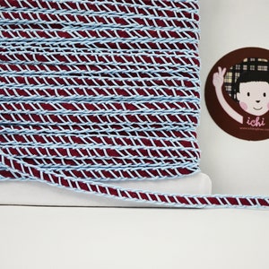 May include: A spool of burgundy and light blue braided trim. The trim has a zig-zag pattern.