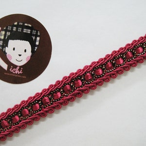 May include: A close-up of a pink and gold trim with a decorative design. The trim is made of fabric and has a woven texture.