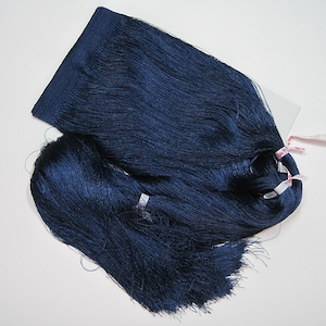 Könnte beinhalten: Ein Bündel marineblauer Fransenborte, mit einem gewebten Oberteil und langen, fließenden Strähnen. Die Borte ist mit kleinen rosa und weißen Bändern gebunden. Geeignet für Bastelarbeiten oder zur Dekoration.
