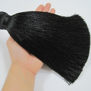 May include: A large black tassel with a long, thick fringe. The tassel is made of a soft, silky material and has a loop at the top for hanging.