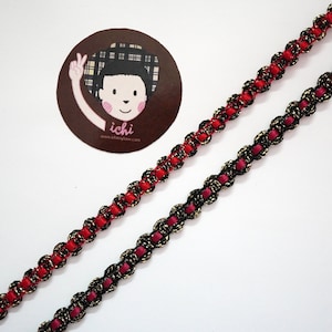 Könnte beinhalten: Zwei geflochtene Besatzschnüre, eine rote und eine schwarze mit goldfarbenem Garn, auf weißem Hintergrund.