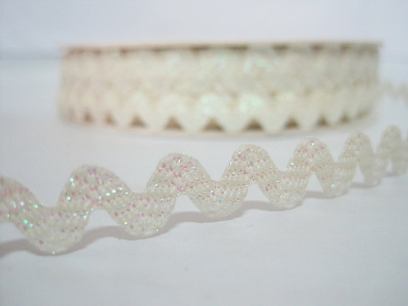 May include: White iridescent glitter trim with a wavy edge. The trim is rolled up on a spool.