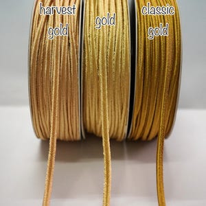 Könnte beinhalten: Drei Spulen goldfarbener Kordel, beschriftet mit "harvest gold", "gold" und "classic gold".