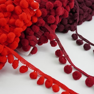 May include: Red and burgundy pom-pom trim with a woven ribbon base. The trim is made of soft, fluffy pom-poms that are attached to a ribbon base.