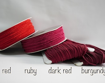 May include: Spools of red, ruby, dark red, and burgundy colored cord. The cord is tightly wound on white spools. The colors are labeled with the corresponding color names in a handwritten font.