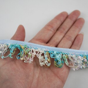 May include: A light blue trim with a fringe of multicolored, iridescent, and textured fabric.