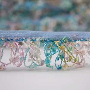 May include: A close-up of a light blue trim with a fringe of colorful threads in shades of pink, blue, green, and gold.