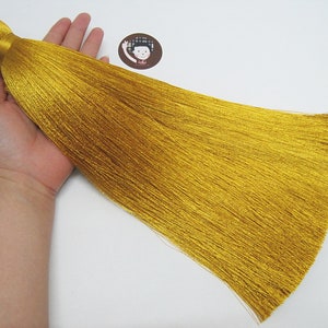 May include: A long, golden tassel with a loop at the top. The tassel is made of many thin strands of yarn and is about 30 cm long.