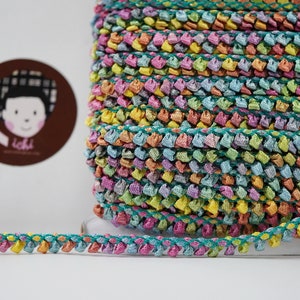 May include: A roll of colourful, multi-coloured, ruffled trim with a teal green base. The trim is made of a soft, textured fabric and has a delicate, ruffled edge.
