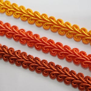 May include: Close-up of three rows of decorative trim in shades of yellow, orange, and brown. The trim has a looped design, creating a textured, ornamental appearance. Ideal for sewing and craft projects.