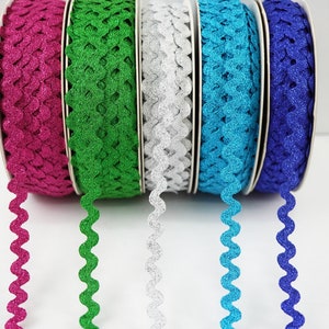 Puede incluir: Cinco carretes de ribete ondulado con purpurina. El ribete es de color rosa, verde, plateado, azul y azul oscuro.