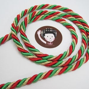 Puede incluir: Borde de cuerda trenzada rojo, verde y dorado. La cuerda está hecha de tres hebras de hilo que se trenzan juntas.