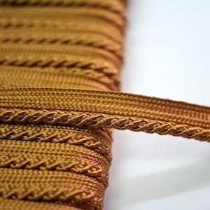 May include: Gold braided trim with a decorative pattern. This trim is perfect for adding a touch of elegance to any project.